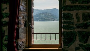 A stone-framed window with a metal railing, offering a view of a calm lake and distant hills. - Castello di Zorzino (Riva di Solto)