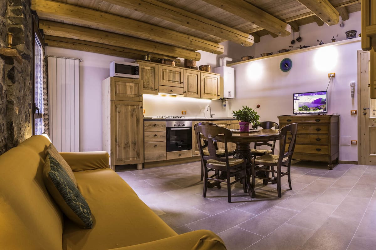 Una cocina acogedora con armarios de madera, una mesa de comedor con sillas y un televisor en la pared.