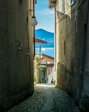 Une ruelle étroite, avec un chemin pavé de pierres, des murs en pierre et une vue sur une montagne et un lac.