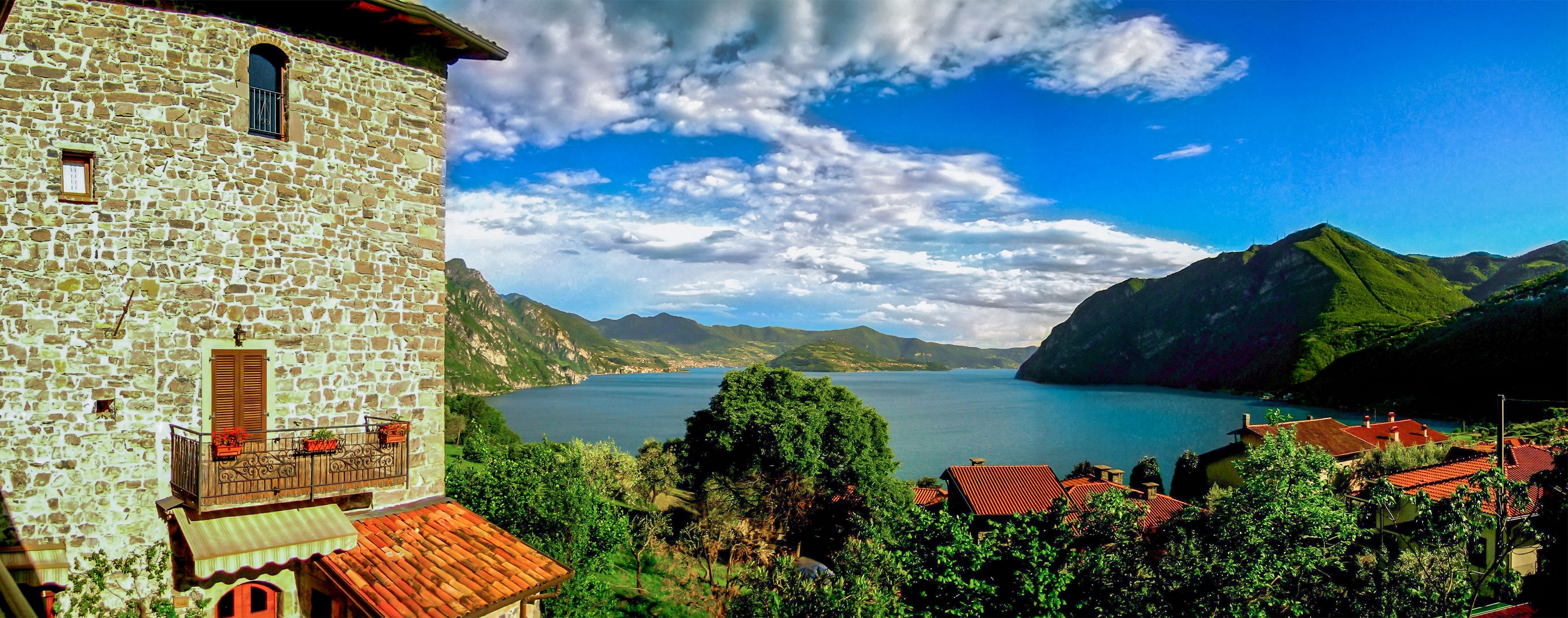 Un edificio de piedra con balcón, vistas a un lago y montañas circundantes.