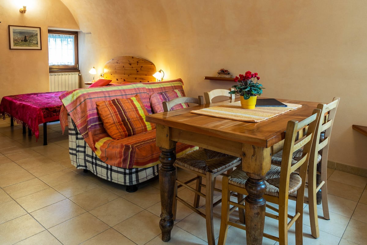 Una habitación acogedora con una mesa de comedor de madera, dos camas con ropa de cama colorida y una ventana con vistas.
