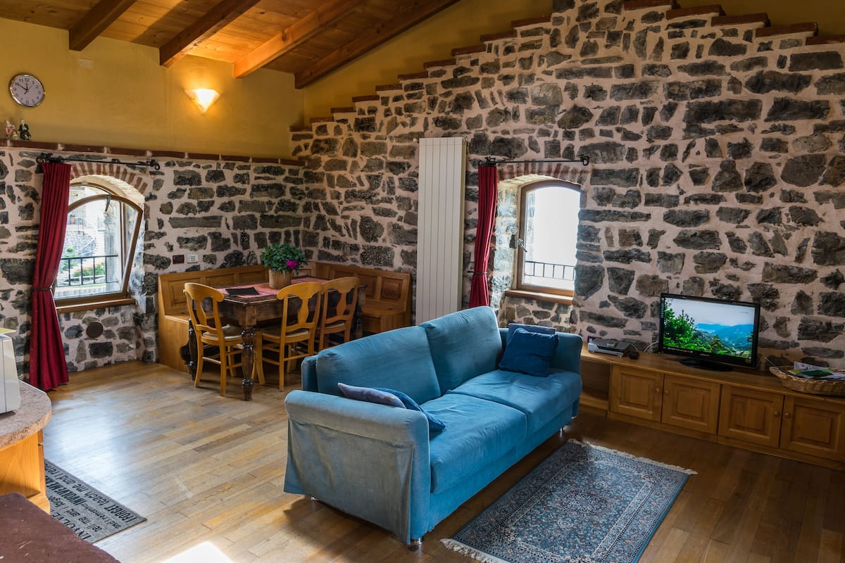 Una habitación acogedora con pared de piedra, un sofá azul, una mesa de comedor de madera y un televisor.