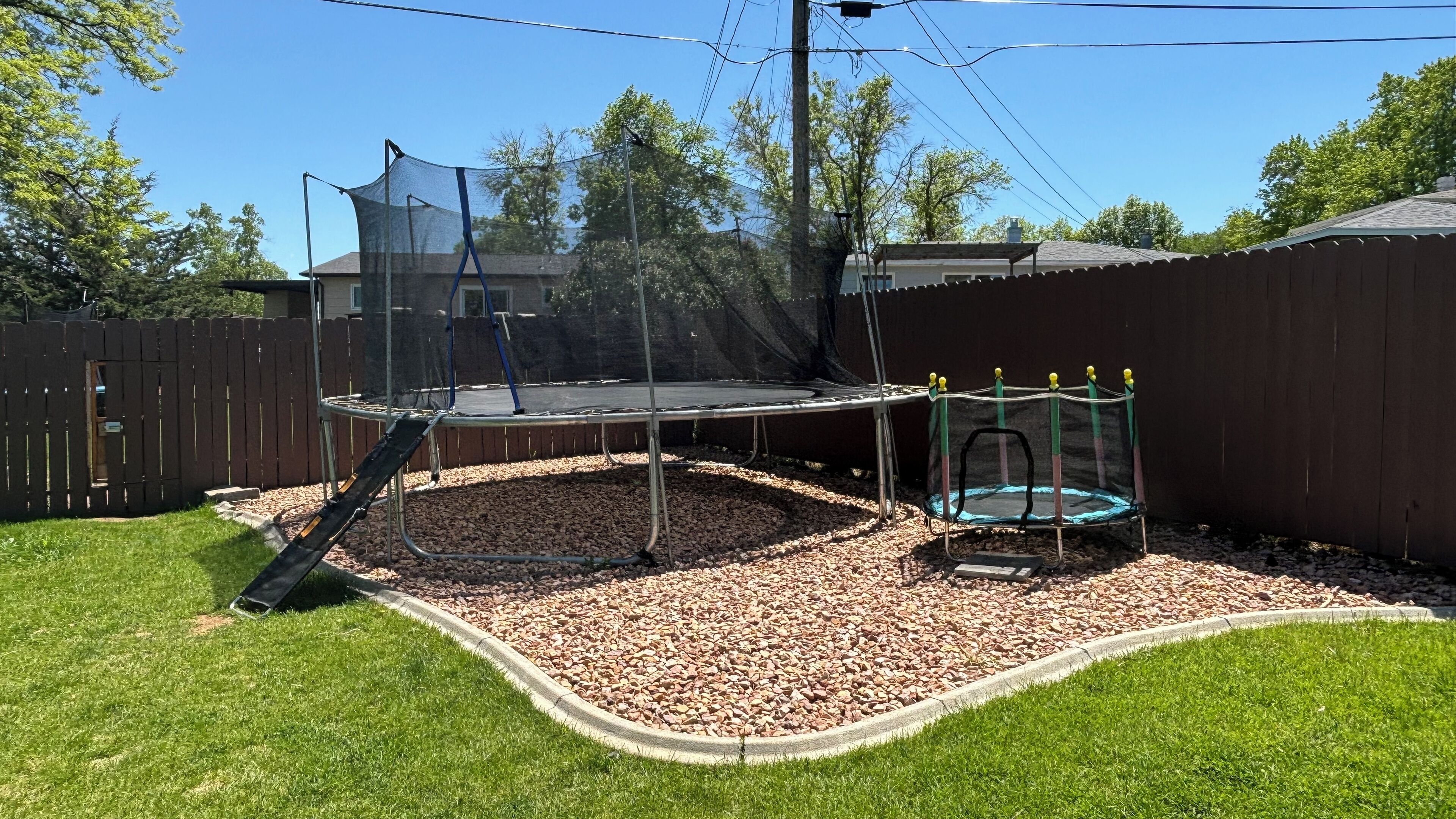 A backyard with a trampoline, a swing set, and a fenced area.