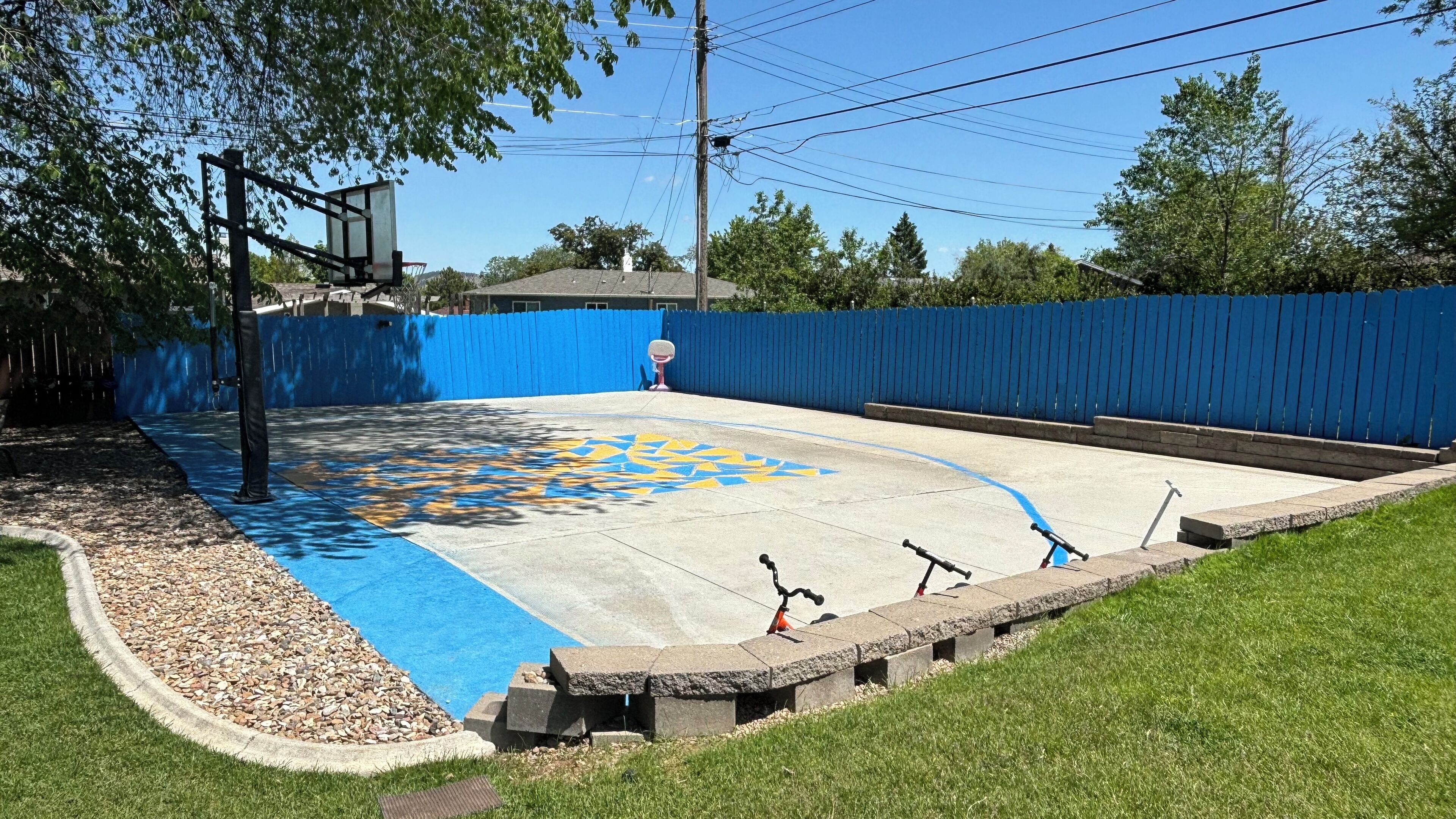 A basketball court with a blue fence, a basketball hoop, and a decorative pattern on the floor.