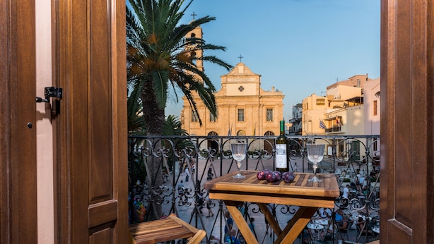 A balcony with a wooden table, two chairs, and a view of a church and buildings in the background. - Casa Irene (Chania)
