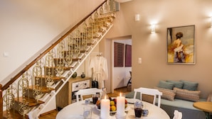 A dining area with a white table set for four, two candles, and a fruit bowl. A staircase with ornate metal railings is visible in the background. - Casa Irene (Chania)