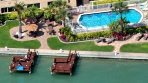 A swimming pool with lounge chairs and umbrellas, surrounded by greenery and a body of water. - Come make a snowman out of sand in warm, sunny Florida! (Treasure Island)