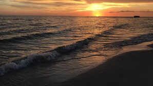 A sunset over the ocean with waves approaching the shore. - Come make a snowman out of sand in warm, sunny Florida! (Treasure Island)