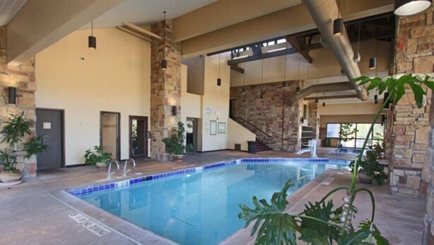 An indoor swimming pool with a tiled edge, surrounded by stone walls and potted plants. - Heart of Rock-n-Roll (2303) | Amazing Views (Brian Head)