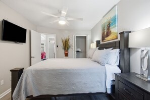 Une chambre à coucher comprenant un lit, un ventilateur de plafond, un téléviseur, un tableau et une porte donnant sur un placard.