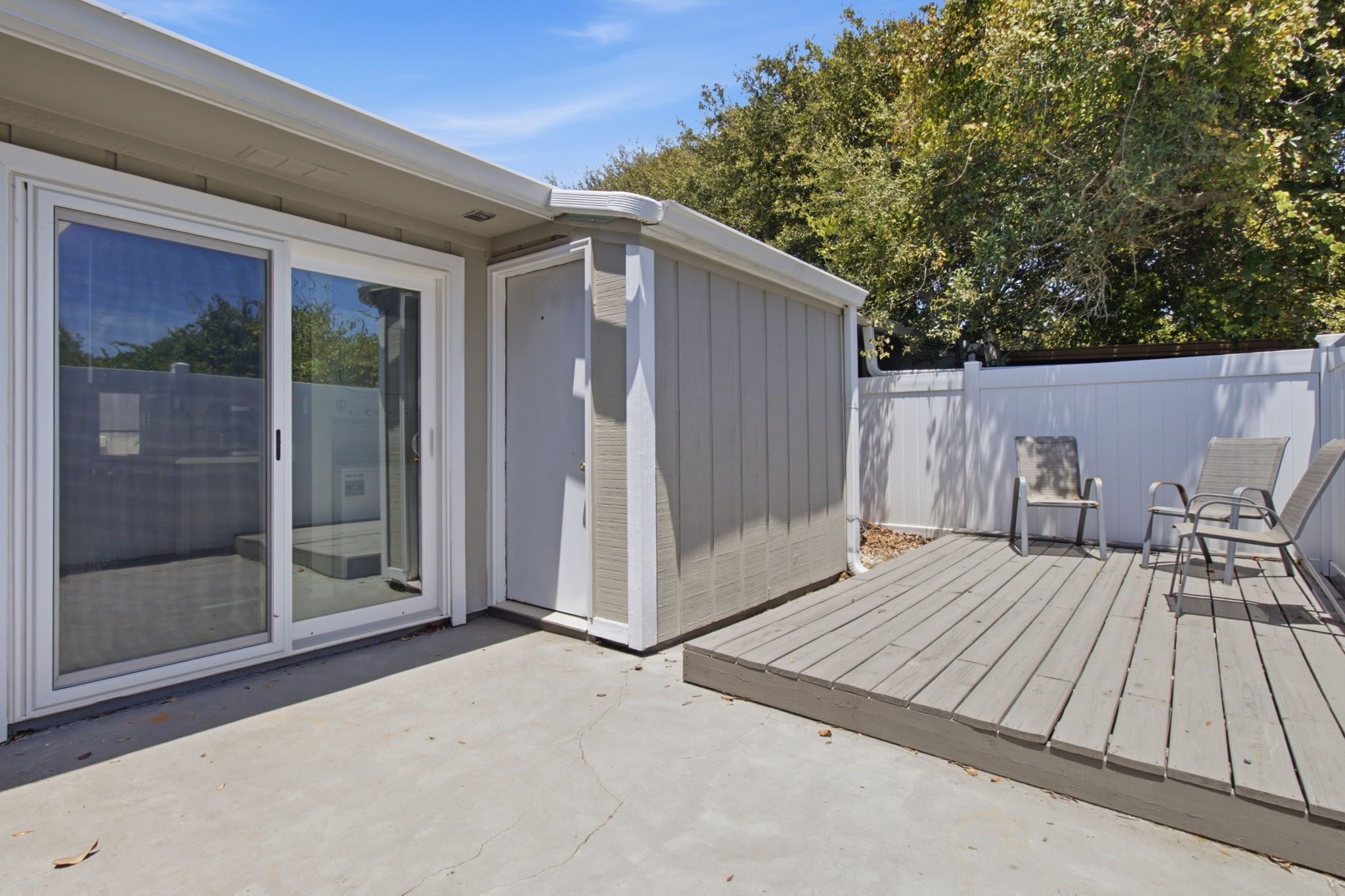Un patio techado con puerta corrediza de vidrio, una pequeña terraza y mobiliario exterior.