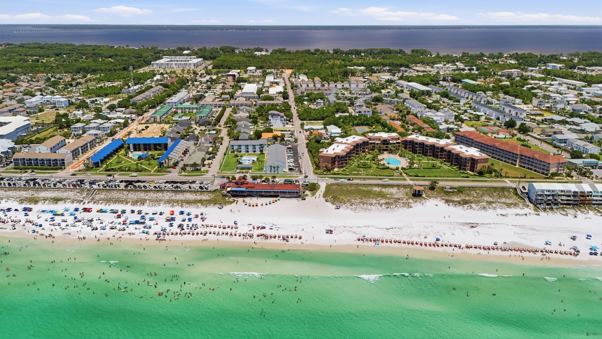 An aerial view of a coastal town with a beach, residential buildings, and a large hotel complex.