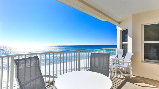 A balcony with a white table and two chairs, overlooking a beach with clear blue water and a bright sky. - Stunning Beachfront Condo w/ Free Beach Service~ Crystal Dunes 405 (Destin)