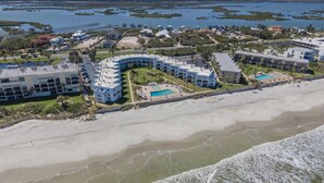 Eine Luftaufnahme eines Küstenhotels mit mehreren Gebäuden, einem Strand und einem Schwimmbad.