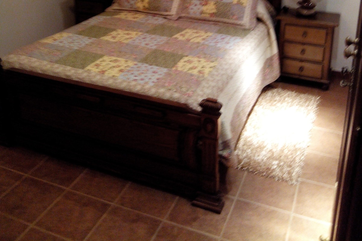 Un dormitorio con una cama de madera, dos mesitas de noche con lámparas y una colcha en la cama.