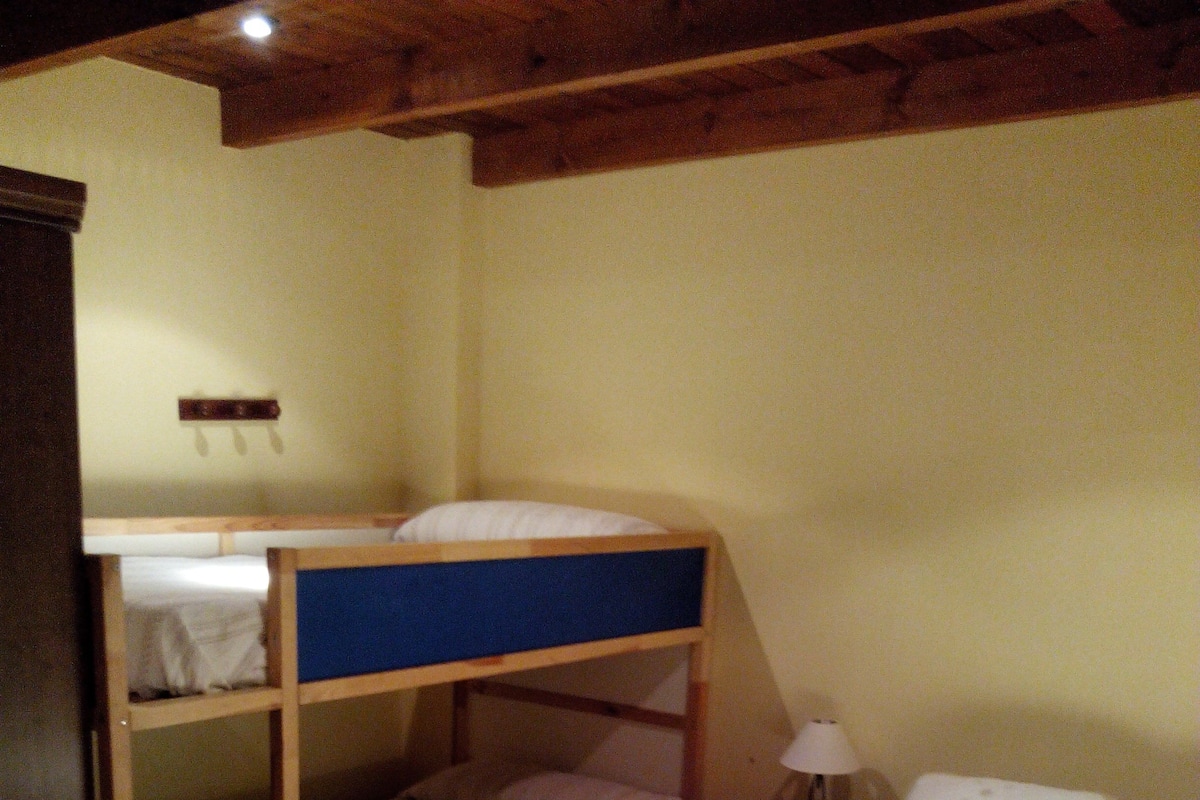 Habitación con literas, cabecera de madera, mesita de noche con lámpara y edredón estampado.