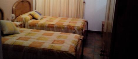 Un dormitorio pequeño con dos camas individuales, cabecera de madera, ventilador de techo y ventana con cortinas.