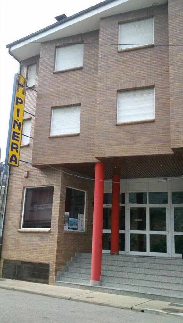 A two-story building with a yellow sign reading "HINERA" on the left side. There are four windows on the second floor and a set of stairs leading to the entrance. - Piñera (Vega de Espinareda)