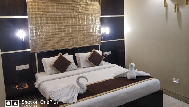 Hotelkamer met een groot bed, twee wandlampen, een decoratieve wandklok en een raam met jaloezieën.