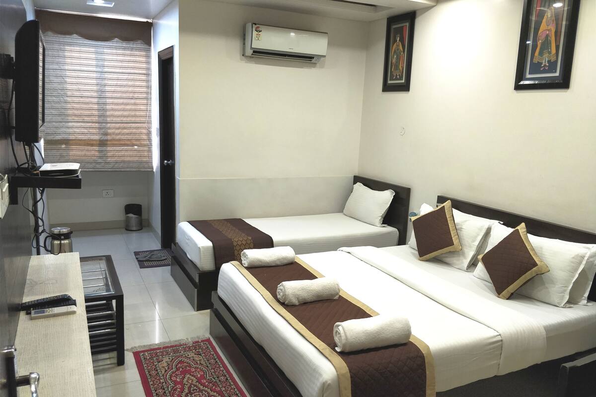 Quarto de hotel com duas camas, uma escrivaninha, uma cadeira, ar condicionado e janela com persianas.