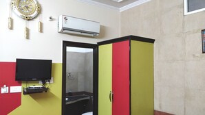 Een badkamer met toilet, wastafel en spiegel. Er is een televisie aan de muur bevestigd en een airconditioning unit boven de spiegel.