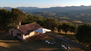 Un edificio de piedra con techo de tejas, mesas al aire libre y vistas a colinas ondulantes y montañas.