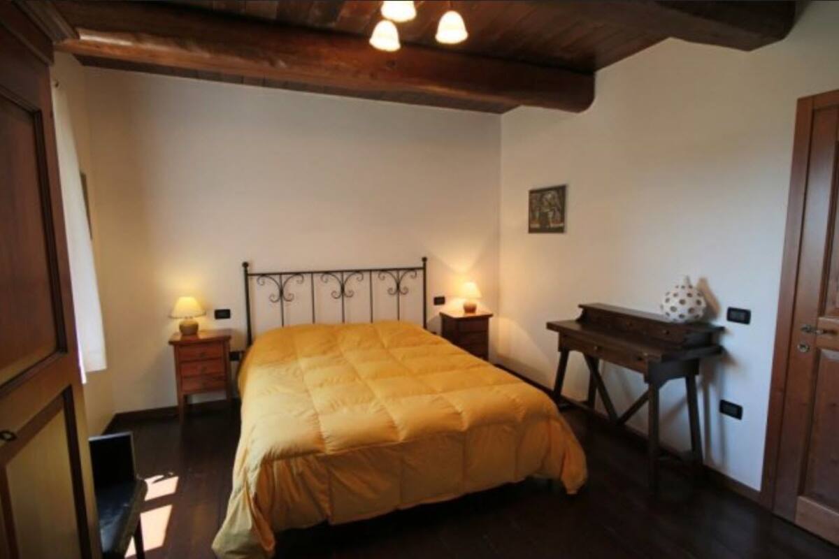 A bedroom with a bed, bedside tables, a desk, and a wooden ceiling.