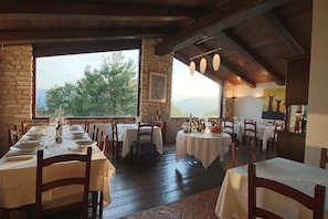 A restaurant with multiple tables set for dining, stone walls, and a view of the outdoors. - Agriturismo Valdifiori (Sassoferrato)