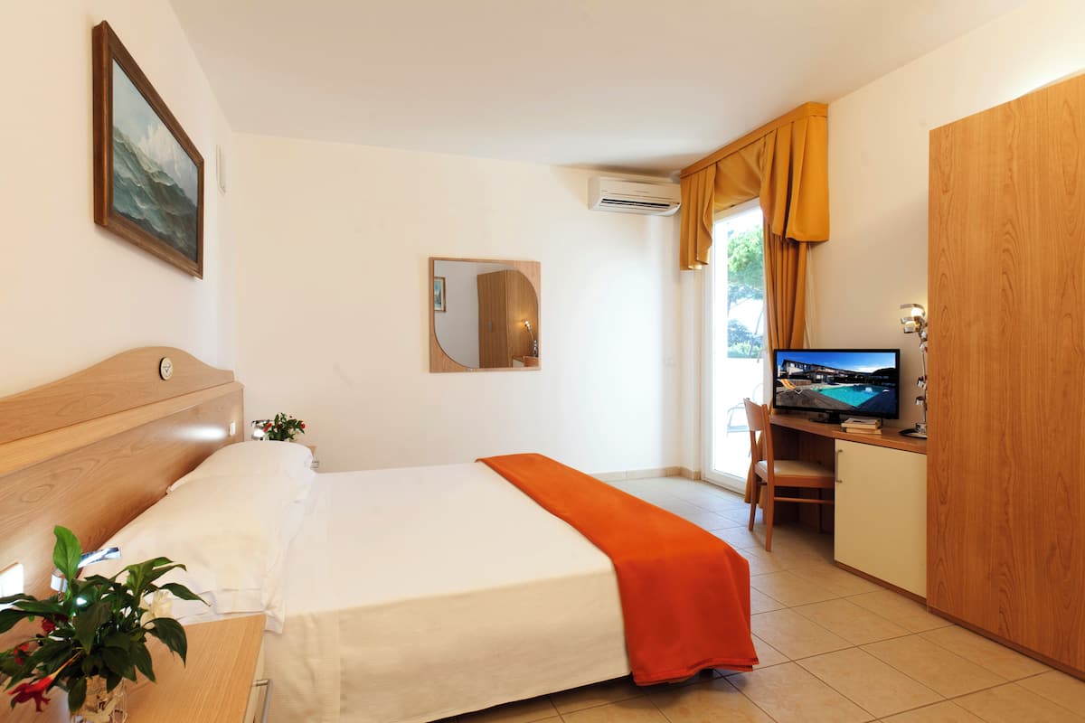 A hotel room with a bed, a desk with a computer, a TV, a mirror, and a window with curtains.