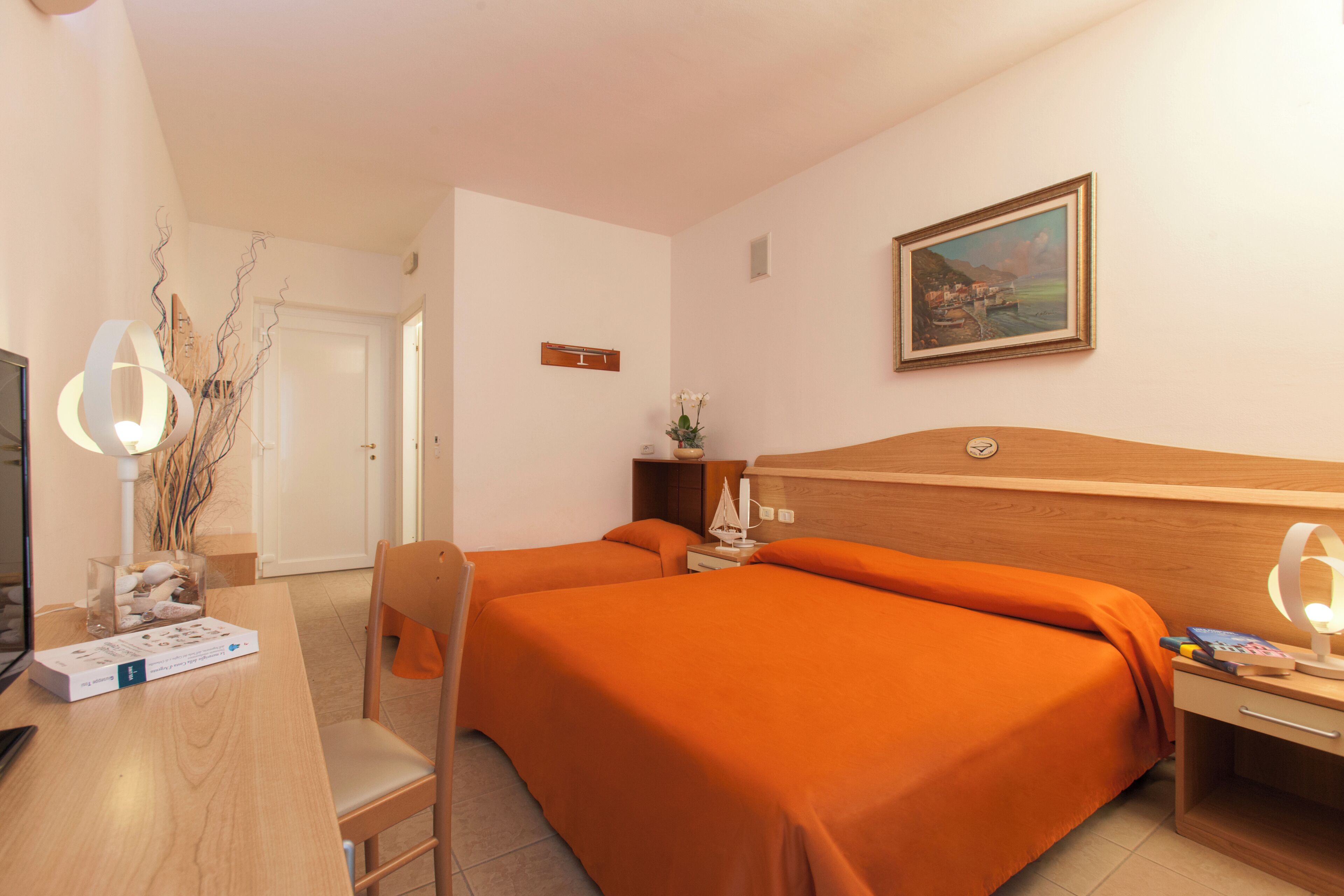 Une chambre d’hôtel avec deux lits, un bureau avec un ordinateur, une chaise, une table de chevet avec une lampe et un tableau au mur.