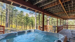 A hot tub area with a wooden deck and a view of a forest. - The Reinerheim Cabin Centrally Located and Close To Lake Pactola (Rapid City)