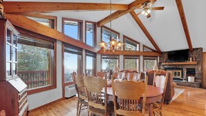 A dining area with wooden chairs and a table, large windows, and a fireplace. - The Reinerheim Cabin Centrally Located and Close To Lake Pactola (Rapid City)