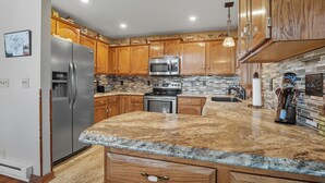A kitchen with wooden cabinets, stainless steel appliances, a granite countertop, and a hanging light fixture. - The Reinerheim Cabin Centrally Located and Close To Lake Pactola (Rapid City)