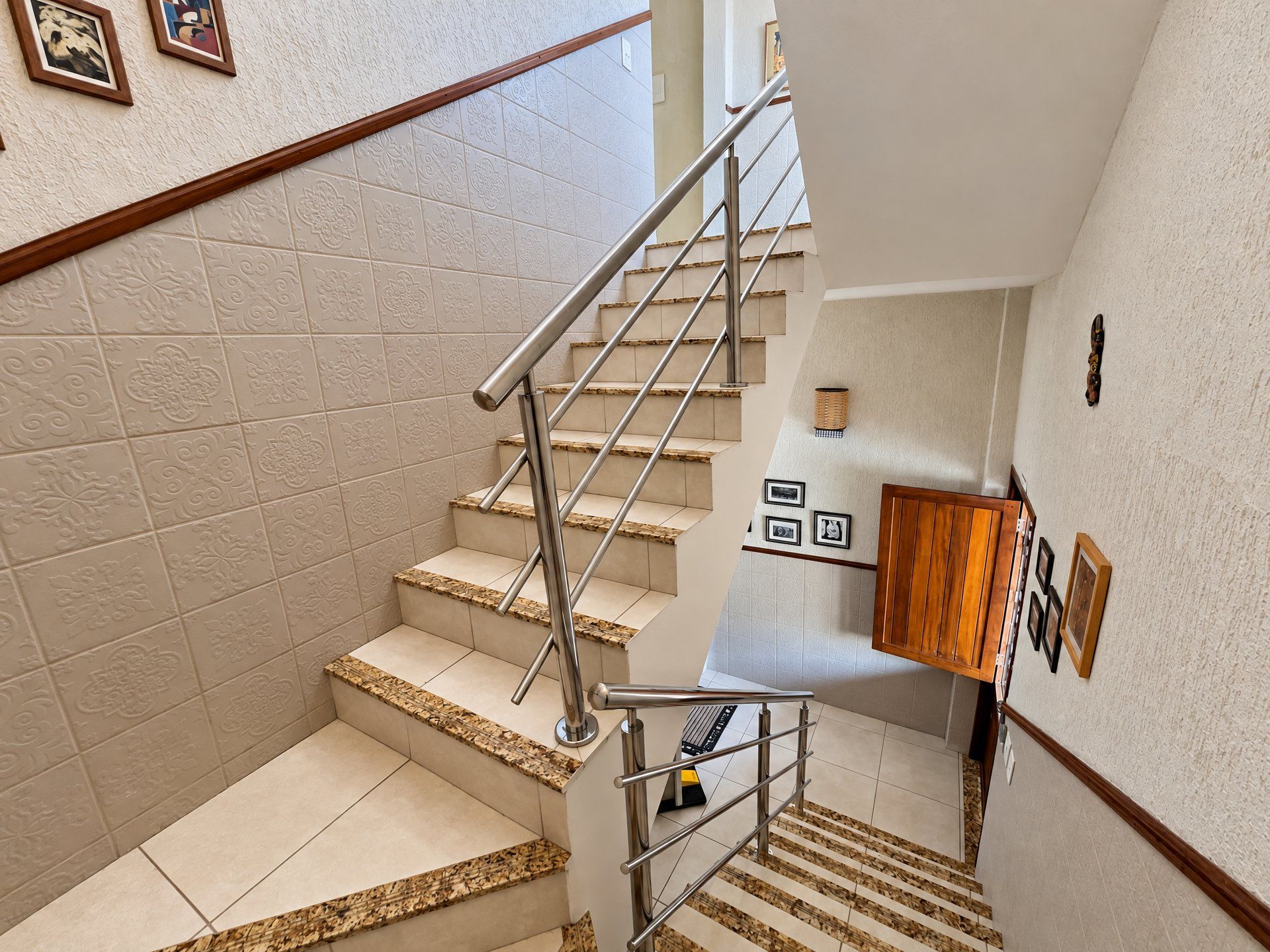 Una escalera con barandilla de metal, paredes de color beige con diseño y una puerta de madera al final.