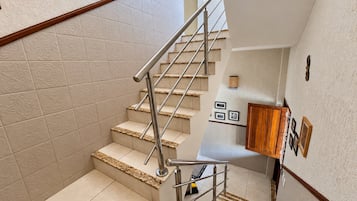Una escalera con barandilla de metal, paredes de color beige con diseño y una puerta de madera al final.