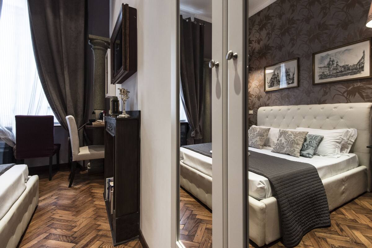 A hotel room with a large bed, a desk, a chair, and a wardrobe.