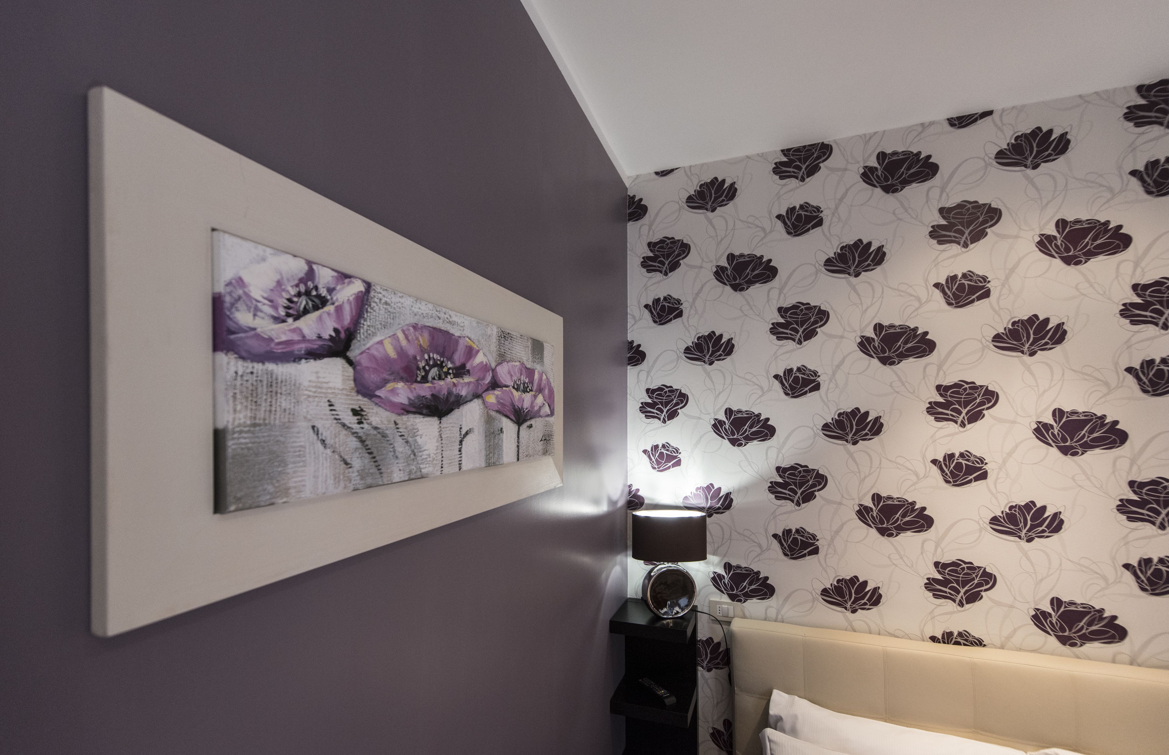 A bedroom with a bed, a wall-mounted mirror, and a floral-patterned wallpaper.