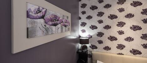 A bedroom with a bed, a wall-mounted mirror, and a floral-patterned wallpaper.