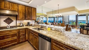 A modern kitchen with wooden cabinets, granite countertops, and a stainless steel dishwasher. - 2BR ocean and sunset views in Mauna Lani point (Kamuela)