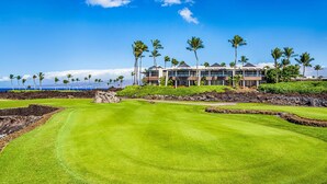 A golf course with a view of a modern building with multiple stories and a pool area. - 2BR ocean and sunset views in Mauna Lani point (Kamuela)