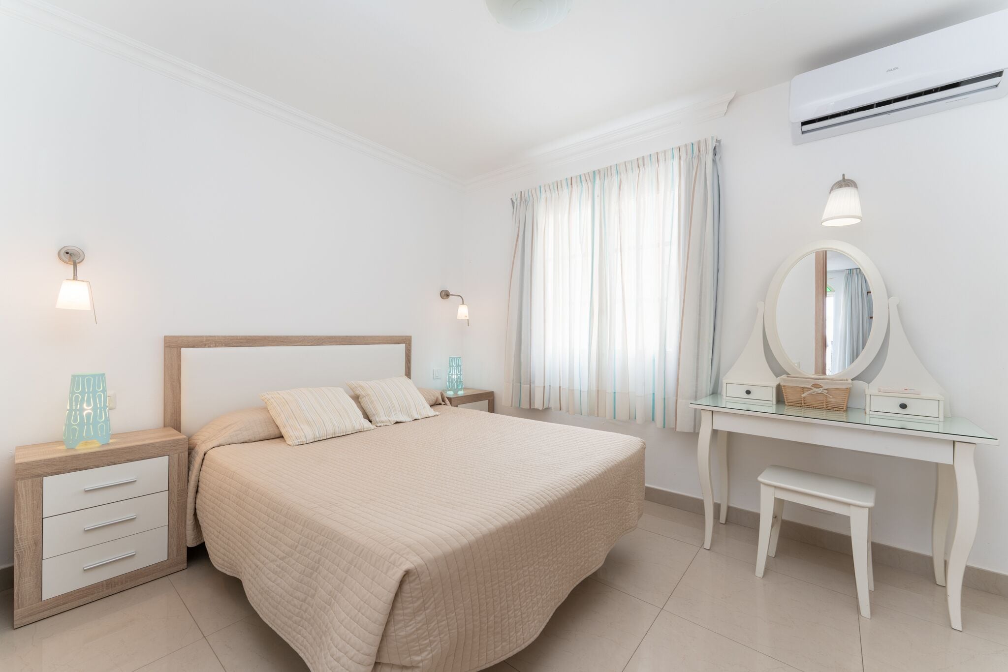Une chambre à coucher comprenant un lit, des tables de chevet, une commode, un miroir et un appareil de climatisation.