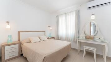 A bedroom with a bed, bedside tables, a dresser, a mirror, and an air conditioning unit.