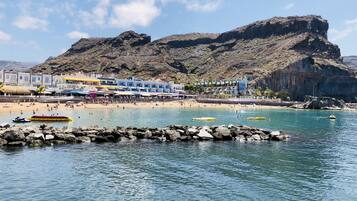 A coastal hotel with multiple floors, a beach, and rocky cliffs in the background.