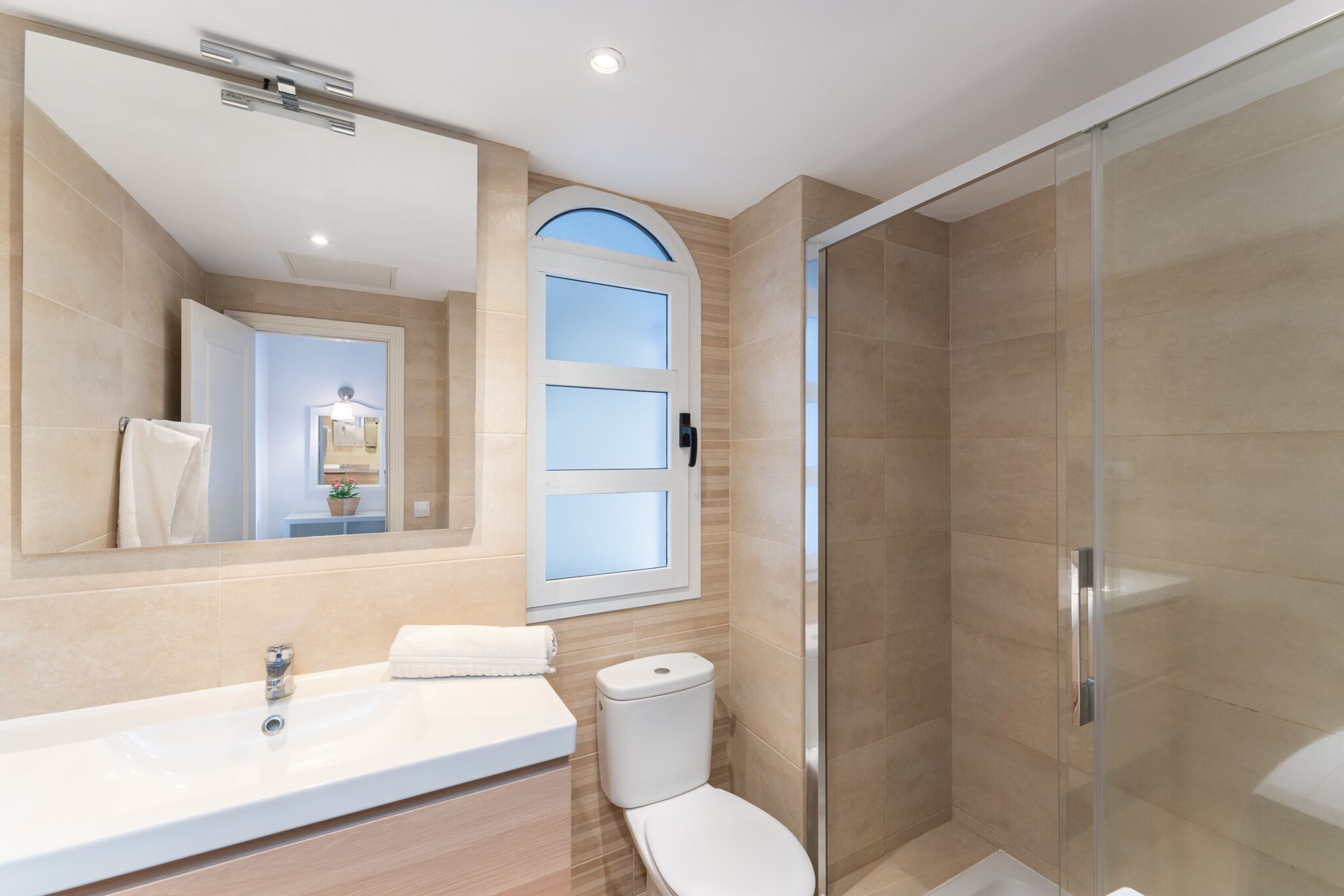 A modern bathroom with a large mirror, a sink, a toilet, and a glass-enclosed shower.