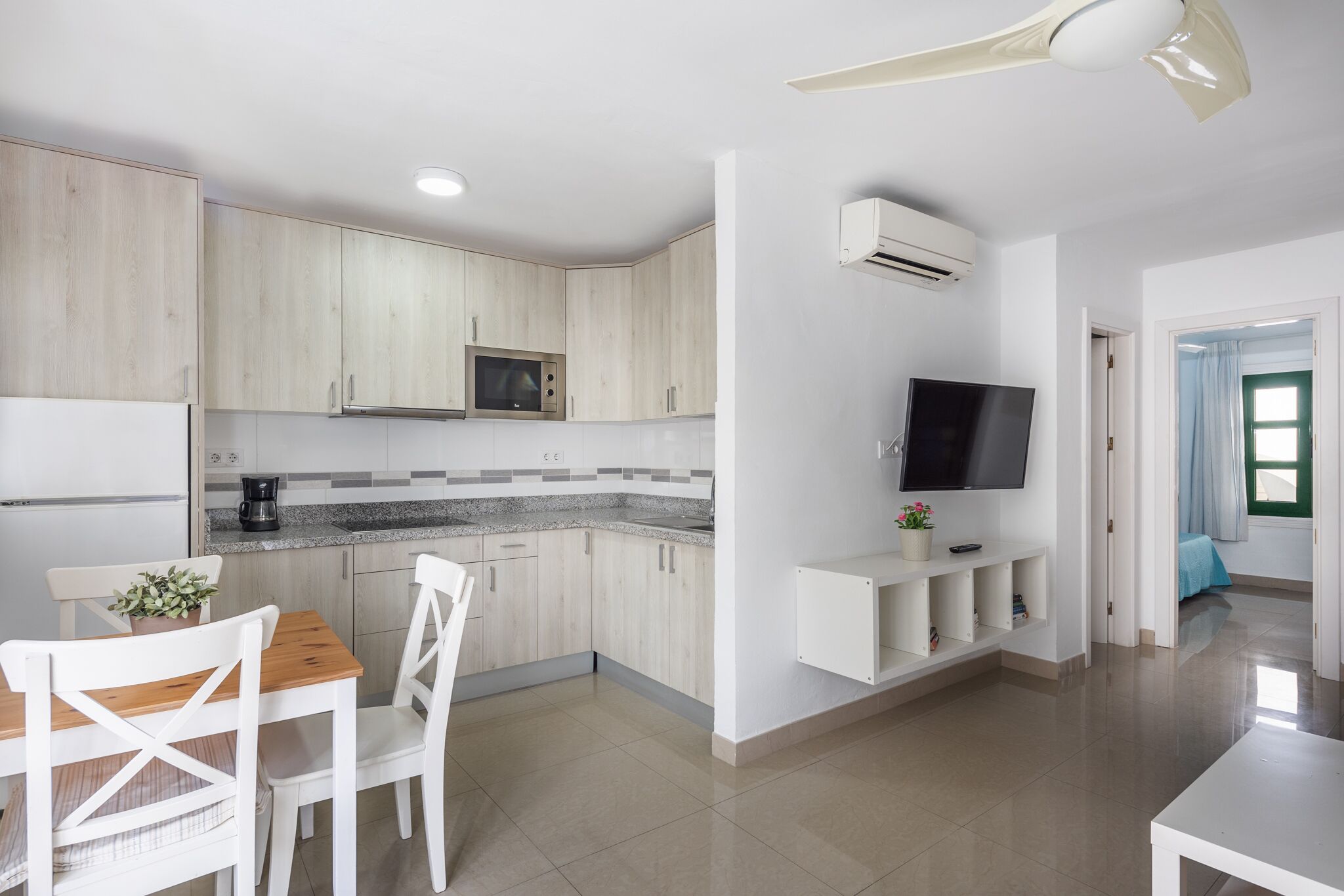 A modern kitchen with white cabinetry, a built-in microwave, and a flat-screen TV mounted on the wall.