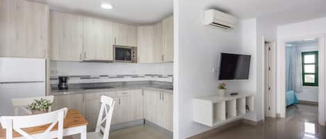 A modern kitchen with white cabinetry, a built-in microwave, and a flat-screen TV mounted on the wall.