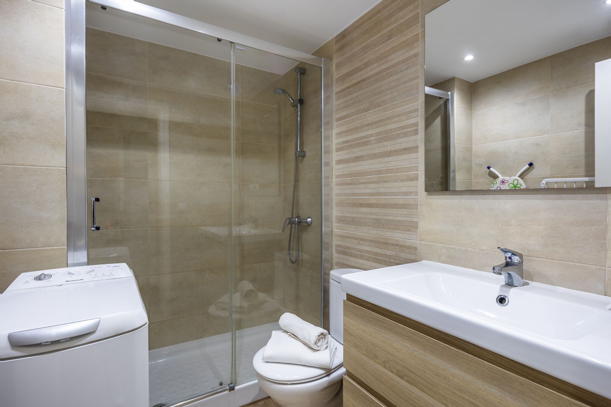A modern bathroom with a glass-enclosed shower, a white toilet, and a large sink with a mirror above it.