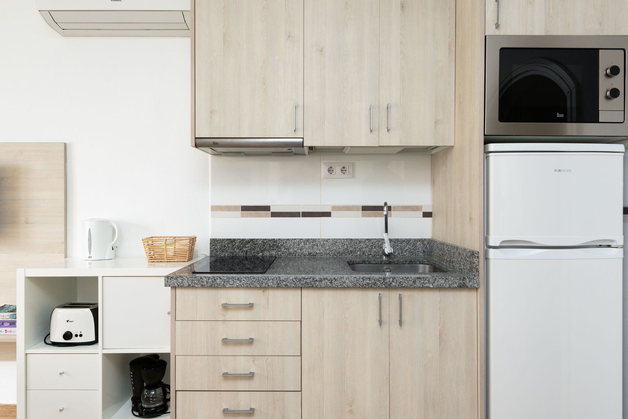 A modern kitchen with light wood cabinets, a granite countertop, a built-in microwave, and a white refrigerator.