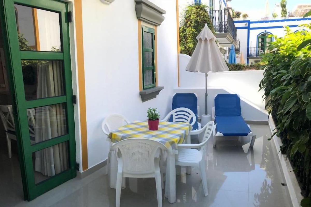 Une terrasse avec une table et des chaises, une plante en pot et une chaise bleue.