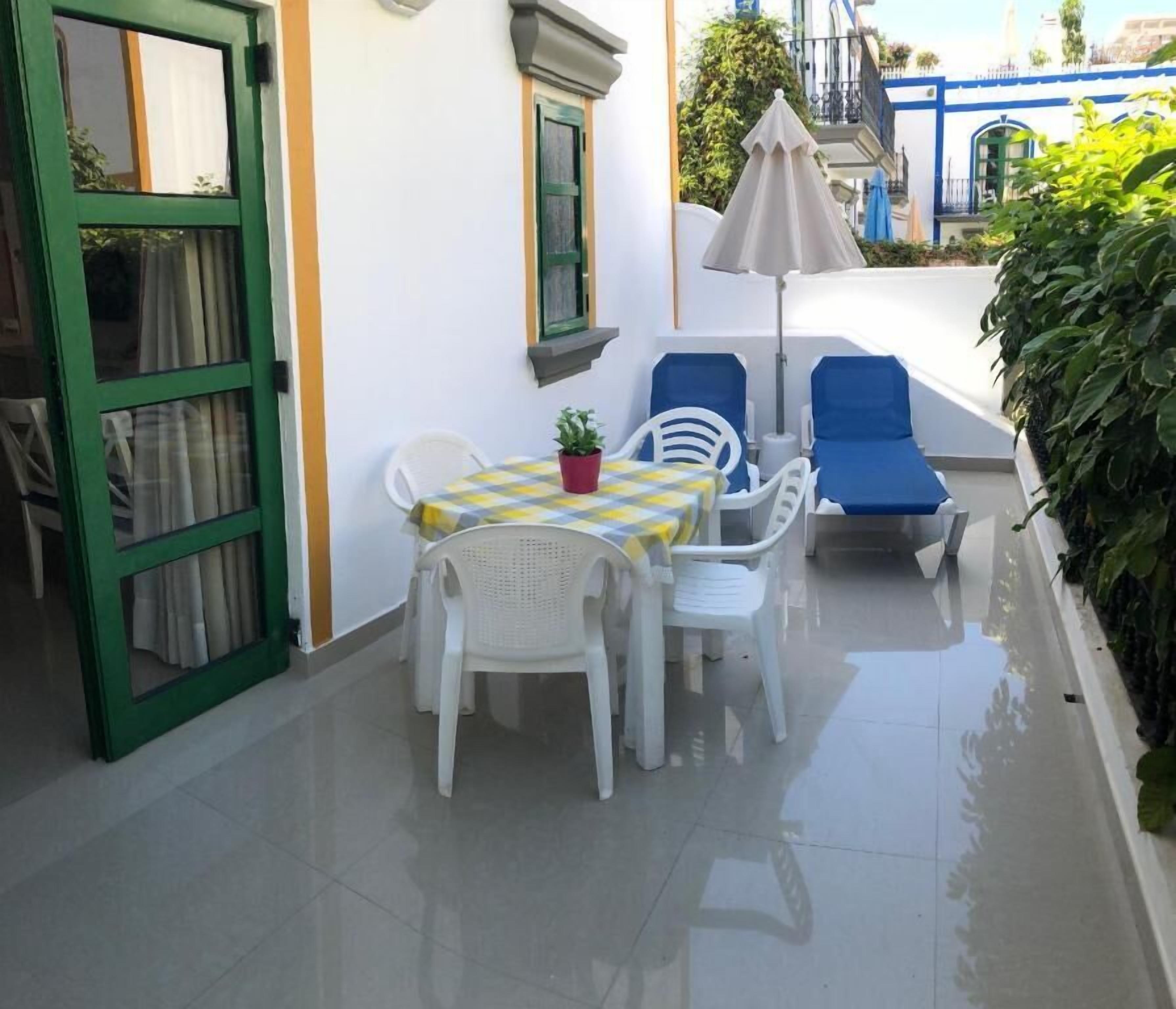 Un piccolo patio con tavolo e sedie, una pianta in vaso e una porta verde.